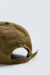 Gorra de seis paneles confeccionada en tejido de algodón con visera de efecto ante en contraste. Presenta un bordado frontal con el texto 'Freedom in every stiff born since 1934' y ajuste regulable en la parte posterior.