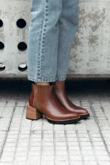 Bota corta de cuero color marrón, con diseño de texturas combinadas en los laterales y elástico. Presenta un taco medio de madera y suela de goma negra.