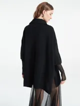 Poncho tejido de punto color negro con escote en V y cuello tipo polo. Presenta un diseño holgado con mangas tres cuartos.