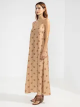 Vestido largo de corte fluido con escote en V profundo y finos breteles. Presenta un estampado animal print combinado con rayas y un detalle decorativo de flor en cobre en el centro del escote.