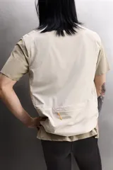 Chaleco técnico de corte regular con cuello subido y cierre frontal de cremallera. Presenta un diseño ligero con panel frontal ligeramente acolchado, bolsillos laterales con cremallera oculta y un bolsillo adicional en el pecho con tirador en color naranja. Incluye acabados con cinta elástica en el bajo y detalle de logo estampado.