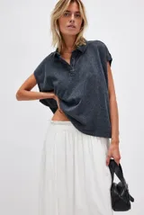 Remera estilo polo de corte amplio color gris oscuro, con cuello clásico y botonadura corta en el frente. Tiene mangas cortas con dobladillo y aberturas laterales en el ruedo que aportan comodidad y un calce relajado.