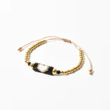 Pulsera ajustable con cuentas doradas y detalle central tejido con cuentas negras, blancas y doradas.