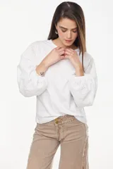 Blusa blanca de calce recto y relajado, con mangas largas abullonadas de broderie y puños ajustados.