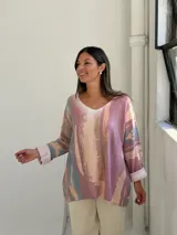 Sweater de punto con diseño abstracto en tonos rosados, beige y azul, de corte holgado, cuello en V y mangas largas con puños vueltos.