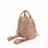 Mochila de diseño acolchado en color beige, con compartimento principal y bolsillo frontal con cierre. Presenta asas superiores de mano y correas ajustables, con un detalle de llavero colgante con cuentas decorativas.