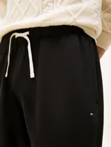 Pantalón de jogging negro de corte regular, confeccionado en felpa aterciopelada de mezcla de algodón y poliéster. Presenta cintura con cordón, bolsillos laterales y trasero, y bajos elásticos. Incluye logo de Tommy Hilfiger bordado en el muslo.