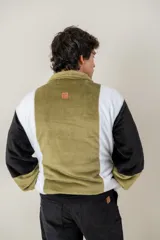 Buzo de textura afelpada con diseño de bloques de color en verde, blanco y negro. Presenta cuello alto con cierre de botones a presión y bolsillos laterales.
