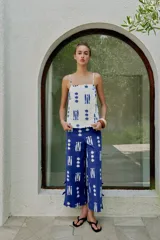 Top de escote recto con tirantes finos ajustables, estampado con motivos marinos de peces y conchas en color azul sobre fondo blanco. Presenta detalle de botones decorativos en el frente y aberturas en el bajo.