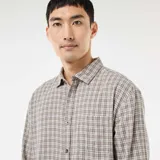 Camisa de manga larga con estampado de cuadros en tonos beige y marrón, confeccionada en franela de algodón. Presenta cuello clásico, cierre frontal con botones y un bolsillo en el pecho.
