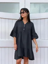 Vestido corto de lino color negro, con cuello mao y escote con botones de nácar. Presenta mangas cortas con volados y un ruedo inferior con volado.