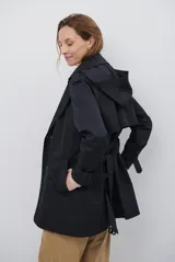 Trench coat negro de corte midi, con cuello solapa, cierre frontal cruzado con botones y cintas ajustables en los puños.