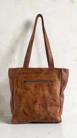 Cartera tipo tote de cuero color marrón terra, con diseño pintado a mano en el frente y borlas decorativas colgantes.