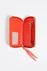 Billetera de estructura rígida Bimba y Lola, color naranja, con cierre de cremallera y tirador de cordón. Presenta el logo de la marca grabado en dorado en el frente.