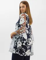 Conjunto de tres piezas compuesto por una musculosa de silueta recta, un pantalón de seda fría con caída fluida y cintura elastizada, y un kimono de tul con bordado floral, frente abierto y mangas acampanadas. Incluye collar largo removible.