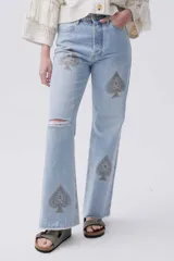 Jean celeste de calce recto y tiro medio-alto, con bordado de picas en tonos amarronados, lavado claro y ruedo desflecado.