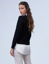 Buzo combinado con torso de tejido de punto fino en color negro y detalles de cuello y ruedo en gasa blanca que simulan una camisa debajo. Presenta escote en V y mangas largas.