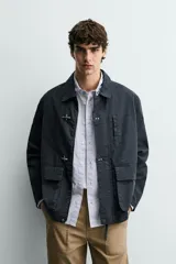 Parka de corte relajado confeccionada en mezcla de algodón color marrón. Presenta cuello solapa, cierre frontal con cremallera oculta y alamares metálicos, bolsillos de plastrón con solapa en la cadera y bolsillo de vivo en el pecho.