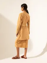Tapado color ocre con cuello camisero, cierre frontal con botones y cinturón de la misma tela. Tiene múltiples bolsillos con solapa y botón en el frente.