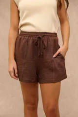 Short marrón con cintura elástica y cordón ajustable, bolsillos laterales y costuras decorativas a la vista.