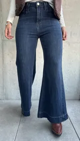 Jean de corte oxford con tiro alto, confeccionado en denim azul oscuro con costuras a tono. Presenta un diseño de pierna ancha y cierre frontal con botón metálico.