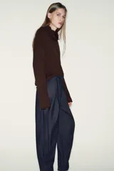 Pantalón de denim azul oscuro, tiro alto, con pinzas delanteras que generan volumen en la cadera y pernera ancha y recta. Presenta cierre frontal y bolsillos laterales.