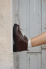 Borcegos de cuero charolado negro con cordones jaspeados en tonos marrones y suela track dentada con costura blanca visible.