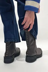 Bota de cuero color chocolate, con caña media, cierre lateral y tachas decorativas en la parte trasera.