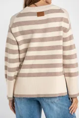 Sweater de punto con diseño a rayas horizontales en color negro y crema. Presenta cuello redondo, mangas largas con puños acanalados y un detalle de borde en tono bronce metalizado en el ruedo y los puños.