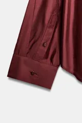 Camisa amplia de cuello solapa con escote en pico y manga larga, en tejido satinado de color bordó. Cuenta con un bolsillo de plastrón en el frente y un diseño holgado.