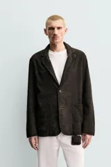 Blazer de corte relajado confeccionada en piel con acabado de ante. Presenta cuello con solapas de muesca, cierre frontal de dos botones, mangas largas y bolsillos de plastrón en la cadera. El diseño no posee forro interior y cuenta con aberturas en la parte trasera.