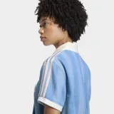 Remera de estilo deportivo inspirada en el fútbol, confeccionada en tejido denim de algodón con efecto lavado. Presenta un diseño de rayas verticales sutiles, cuello polo en color blanco, mangas cortas con bordes en contraste y el logo de la marca estampado en el frente.