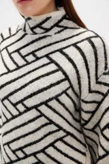 Sweater de tejido jacquard con diseño geométrico de líneas entrelazadas en tonos negro y marrón. Presenta cuello alto, mangas largas con terminación holgada y un corte recto.