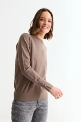 Sweater de punto liso color marrón topo, con cuello redondo y manga larga. Presenta un detalle de tres botones pequeños en la abertura del puño.