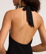 Vestido corto negro de tejido liviano, con escote halter que forma un drapeado (escote degagê) en el busto y ruedo asimétrico con volados.