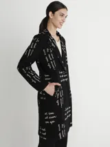 Tapado negro con estampado de texto en color blanco, cuello solapa y cierre frontal con un botón.