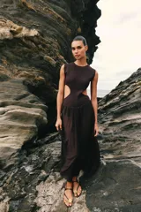 Vestido midi de color negro, sin mangas, con cuello redondo y aberturas laterales en la cintura (cut out). La parte superior es de punto liso y la falda presenta una textura plisada y ligera.