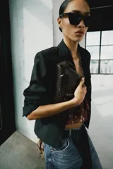 Blazer corto negro de cuello con solapa y manga larga, con hombreras, trabillas en los hombros, falsos bolsillos con solapa en el pecho y en la parte delantera, y cierre frontal con botones.