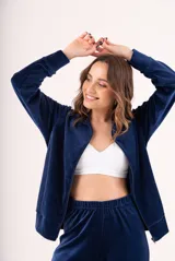 Conjunto de dos piezas confeccionado en tela plush, compuesto por una campera con cierre frontal y cuello alto, y un pantalón de corte recto. Presenta un diseño minimalista y cómodo en color gris claro.