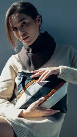 Sobre de mano de símil cuero con diseño de franjas diagonales en negro, blanco y marrón. Cuenta con cierre metálico frontal, bolsillo interior con cierre y otro abierto con división. Incluye correa desmontable para usar como bandolera.