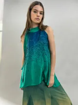 Blusa de satén con escote halter y cuello elevado anudado lateralmente. Presenta un diseño estampado degradado en tonos verde esmeralda y azul, con corte holgado y caída fluida.