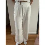 Pantalón palazzo de tiro alto, color blanco, con cierre frontal de doble botón y pinzas en la cintura. Presenta un corte wide leg y bolsillos laterales.