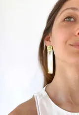 Aros colgantes con base circular dorada y pieza rectangular alargada color hueso.
