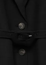 Blazer negro de lino y viscosa, con cuello de solapa, manga francesa, cinturón con hebilla y cierre frontal con botones. Tiene dos bolsillos laterales con solapa.