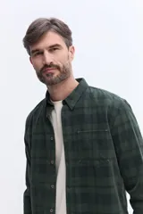 Camisa de manga larga confeccionada en viyela de algodón con diseño a cuadros en tonos verde oscuro. Presenta cuello clásico, cierre frontal con botones y bolsillo aplicado en el pecho.