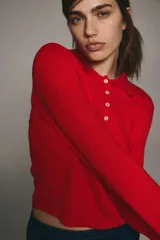 Sweater de punto fino color rojo, manga larga con hombros ligeramente caídos, cuello polo y tapeta de botones. Presenta remates acanalados en puños y bajo.