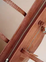 Bolso tote grande de cuero color marrón con textura tipo reptil. Tiene doble asa de hombro, cierre superior y bolsillo frontal con cierre. Incluye un dije colgante en forma de estrella con flecos plateados.