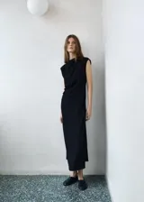 Vestido midi negro sin mangas, con cuello redondo y diseño entallado. Presenta un detalle de fruncido lateral y cierre de cremallera en la parte posterior.