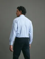 Camisa de vestir de manga larga con diseño de rayas verticales finas en color celeste y blanco. Presenta cuello clásico, cierre frontal con botones y un bolsillo en el pecho.