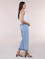 Jean cropped de denim celeste, con tiro alto, pernera ancha y recta, y diseño de cinco bolsillos. Presenta un dobladillo bicolor con flecos en tono más oscuro.